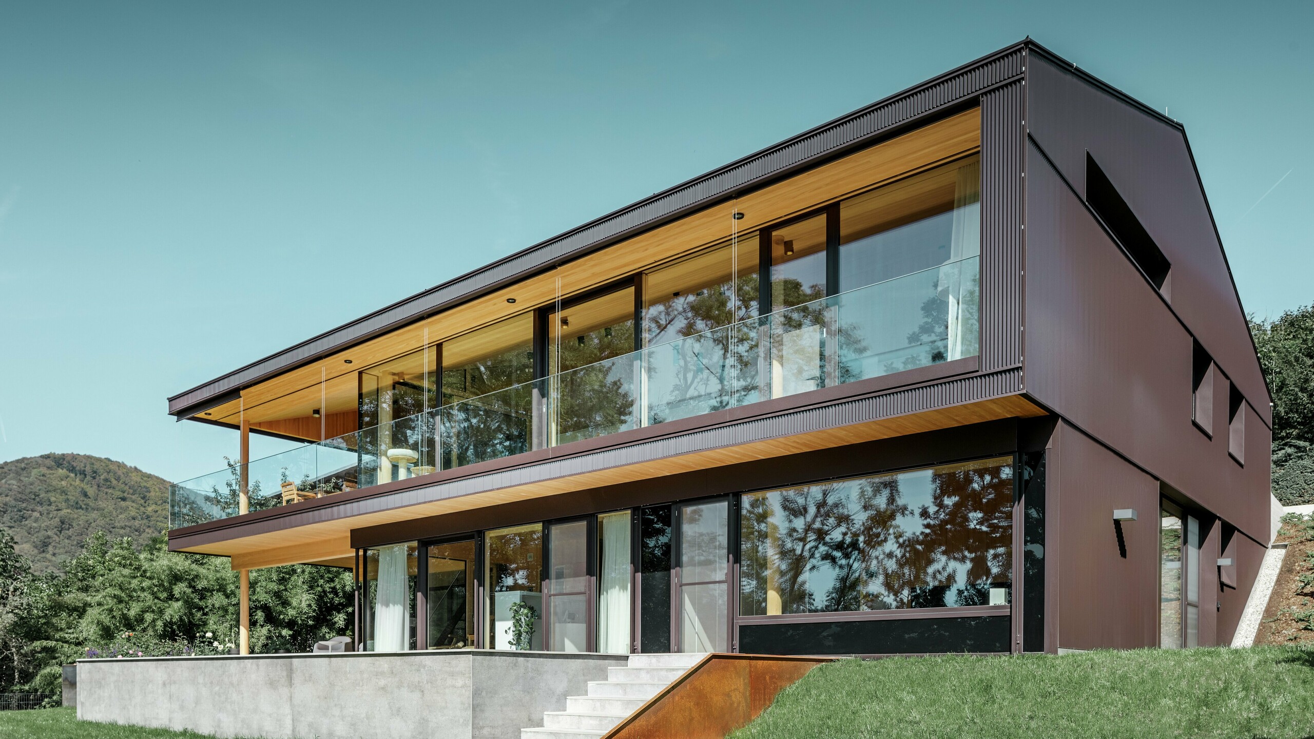 Maison individuelle moderne à grandes fenêtres côté jardin, dont la façade a été recouverte de profils triangle PREFA couleur brun foncé.