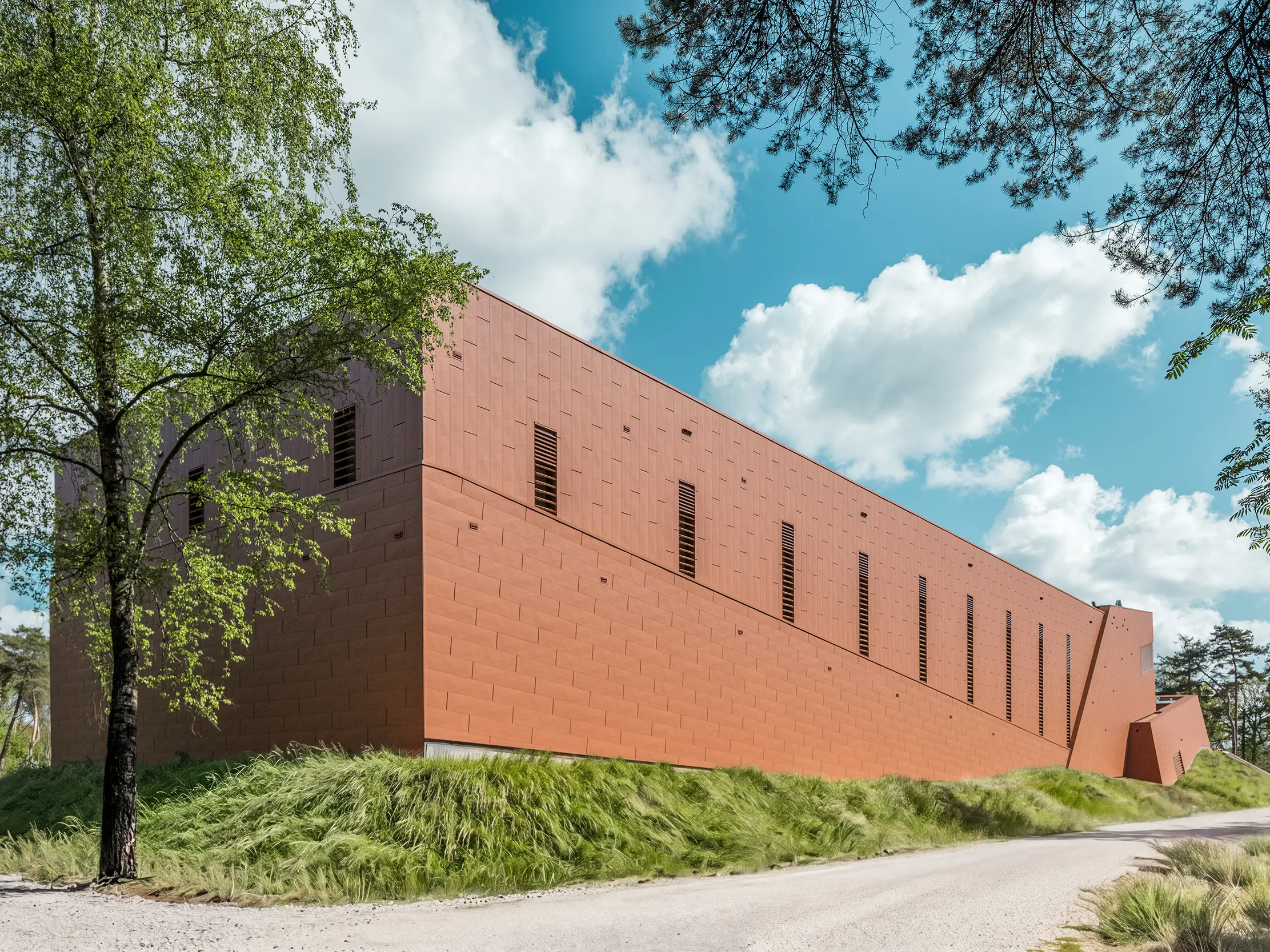 La station de pompage d'eau potable WML, tout en longueur, se dresse fièrement au cœur d'un paysage naturel composé d'arbres, de prairies et d'un ciel panoramique. Sa façade en aluminium PREFA Siding.X, d'une teinte rouille chaleureuse, attire immédiatement le regard et captive tous les visiteurs par sa surface finement facettée et texturée. De fines ouvertures verticales rythment la façade. Durables, légers et recyclables, les panneaux d'aluminium PREFA offrent une résistance maximale aux intempéries, une excellente tenue des couleurs et une enveloppe de bâtiment durable et nécessitant peu d'entretien.