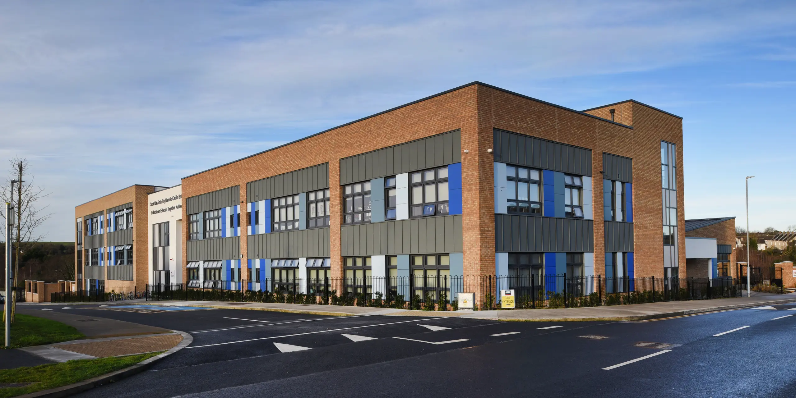 Seitenansicht der Pelletstown Educate Together National School in Dublin. Die hellgraue PREFALZ Stehfalzdeckung bildet eine elegante und witterungsbeständige Außenhaut. Die Aluminiumelemente sorgen für einen harmonischen Übergang zu den Klinker- und Putzfassaden - ein einzigartiger Materialmix.