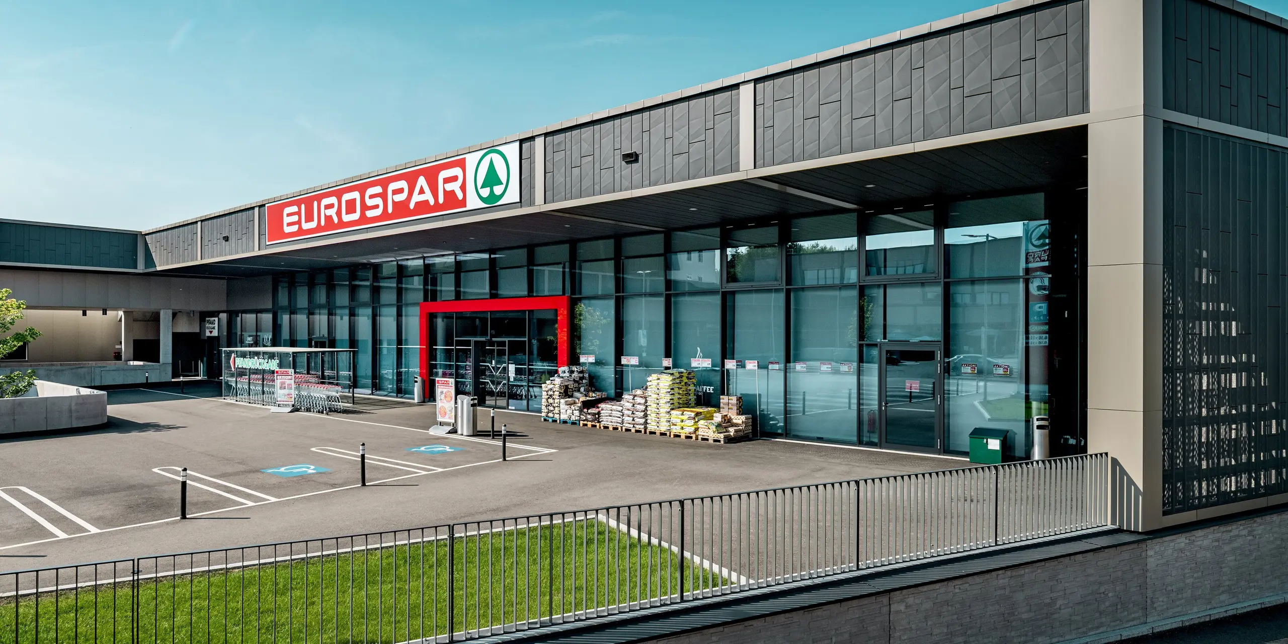 Le supermarché Eurospar de Rohrbach, à la pointe de la modernité, arbore une façade en aluminium signée PREFA. Les panneaux Siding.X anthracite, particulièrement remarquables, confèrent au bâtiment une allure élégante et contemporaine. L'entrée, ornée d'un cadre rouge éclatant, souligne avec élégance le design. La façade, à la structure épurée et jouant avec les ombres et la lumière, offre au bâtiment une apparence moderne et accueillante. L'utilisation des panneaux Siding.X de PREFA garantit un style raffiné, une excellente résistance aux intempéries et un entretien aisé sur le long terme.