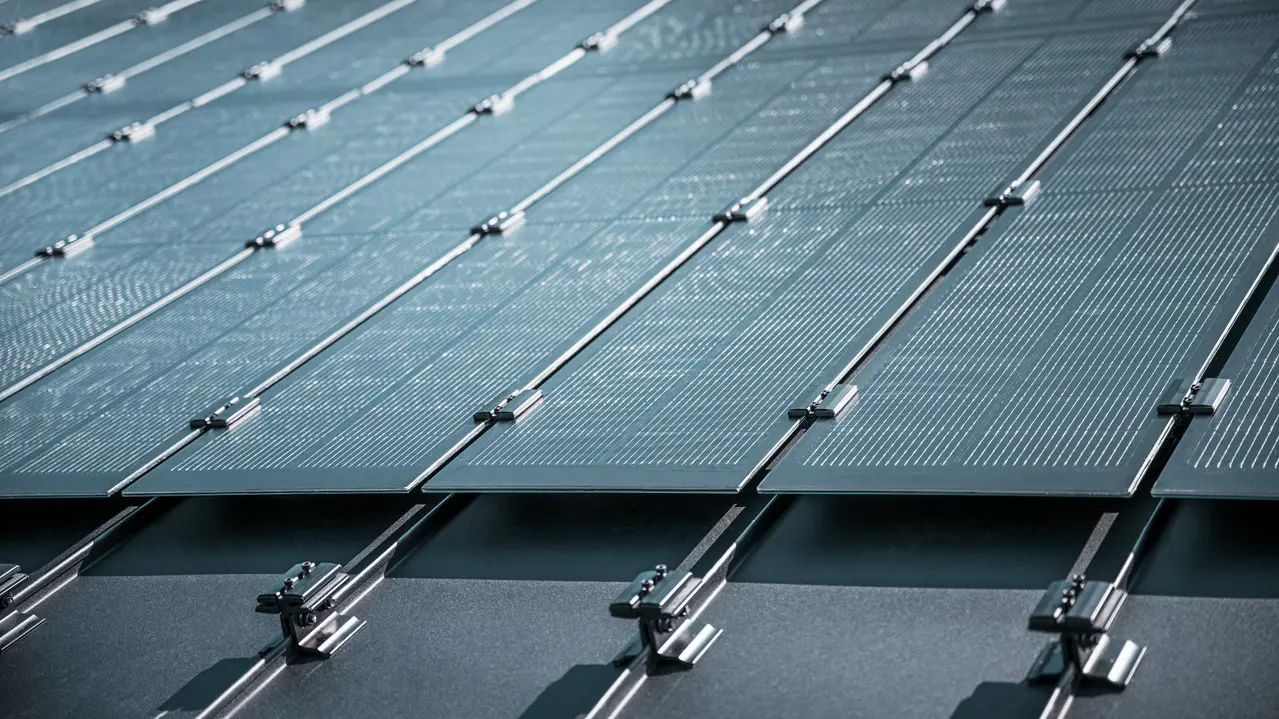Montageansicht mehrerer PREFALZ Solarmodule auf einem bestehenden PREFALZ Dach in Meschede, Deutschland. Die rahmenlosen Glas/Glas-PV-Module sind in präzisen Reihen angeordnet und mit robusten Halterungen fixiert, was eine flächenbündige, elegante Optik erzeugt. Die hochwertige Befestigungstechnik sorgt für Stabilität und Langlebigkeit, während die innovative TOPCon-Zellentechnologie maximale Energieeffizienz garantiert. Das Bild vermittelt modernste Photovoltaik-Lösung, die Design, Funktionalität und Nachhaltigkeit perfekt vereint.