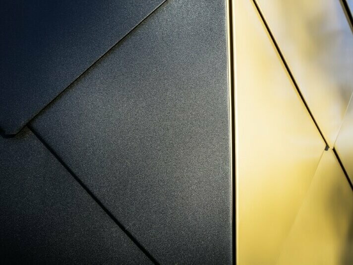 Detailaufnahme des verwendeten PREFA Produkts. Das Gebäude wurde mit der PREFA Wandraute 44 x 44 in den Farben Mayagold und P.10 Schwarz verkleidet.