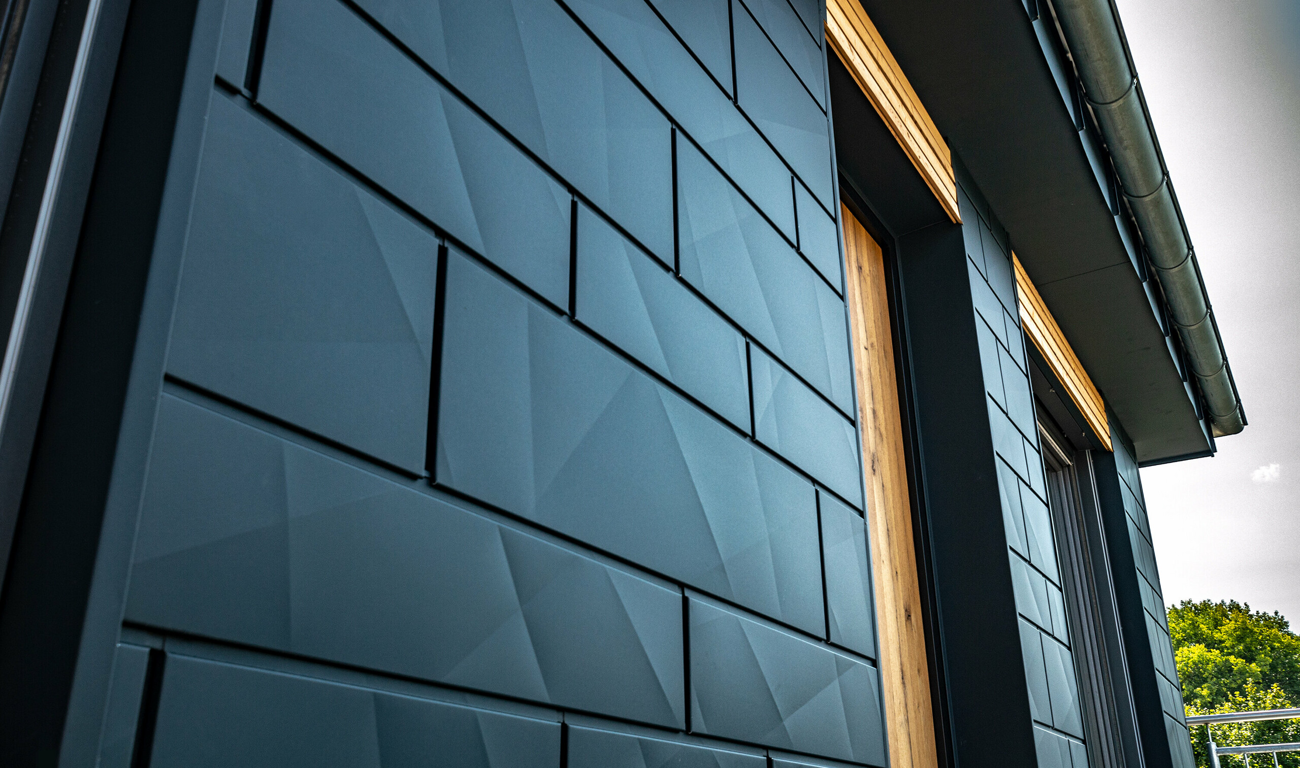 Façade avec le Siding.X PREFA en anthracite, avec portes-fenêtres et grandes baies vitrées, combinée à une façade en bois.