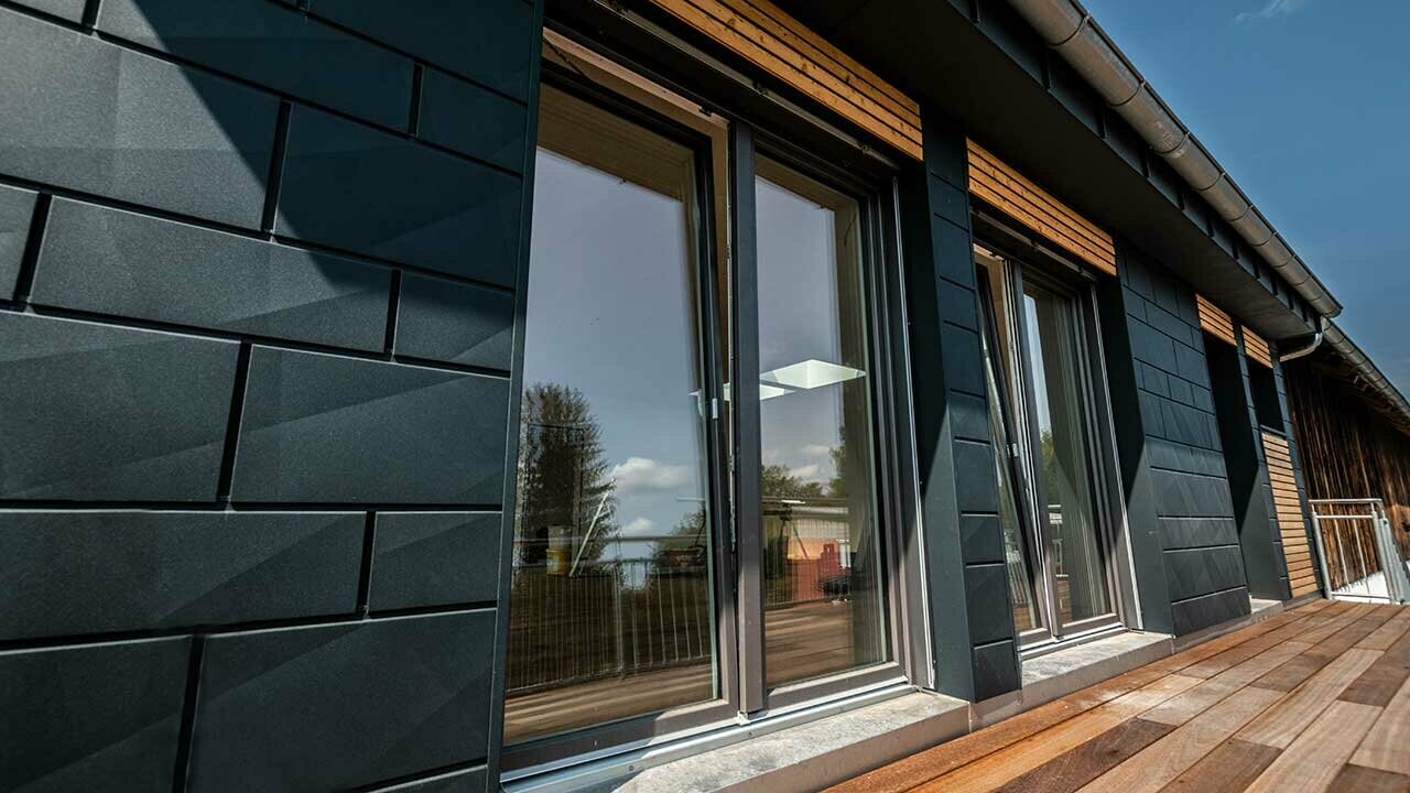 Façade avec Siding.X PREFA couleur anthracite avec portes de balcon et grandes surfaces vitrées mélangées avec un habillage en bois.