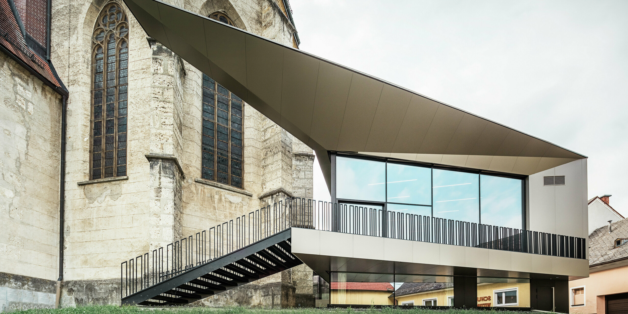 Die Rückseite des Pfarrzentrums in Sierning zeigt die Vielseitigkeit von PREFA Aluminium Verbundplatten in Kombination mit Glas. Die fugenlose Montage und die exakte Kantenausbildung unterstützen die architektonische Idee einer schwebenden Struktur mit hoher Widerstandsfähigkeit gegen äußere Einflüsse.