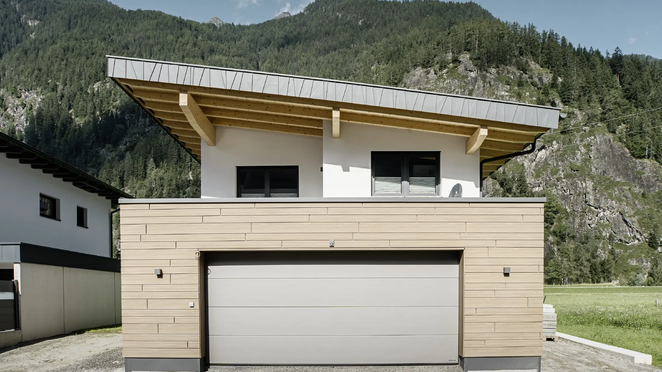 Moderne nieuwbouw met lessenaarsdak en individuele dakrandbekleding, garage met plat dak en aluminium gevel in walnoot van PREFA. De sidings zijn horizontaal geplaatst en hebben verschillende bouwbreedtes.