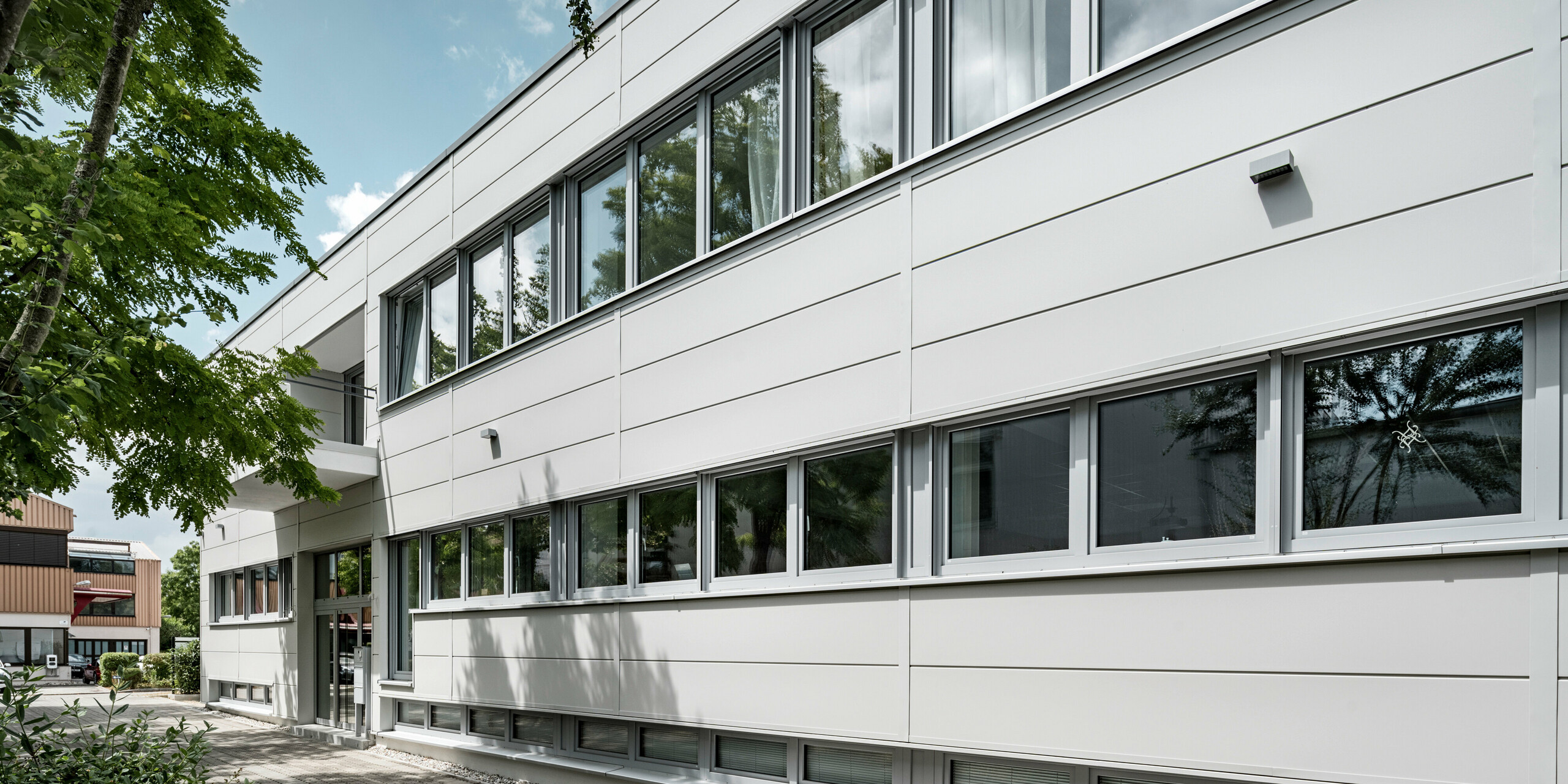 Des Sidings PREFA grand format entourent un bâtiment d'entreprise à Oberschleißheim (Allemagne). Les éléments de façade extra-larges en aluminium ont été choisis dans la couleur blanc Prefa.