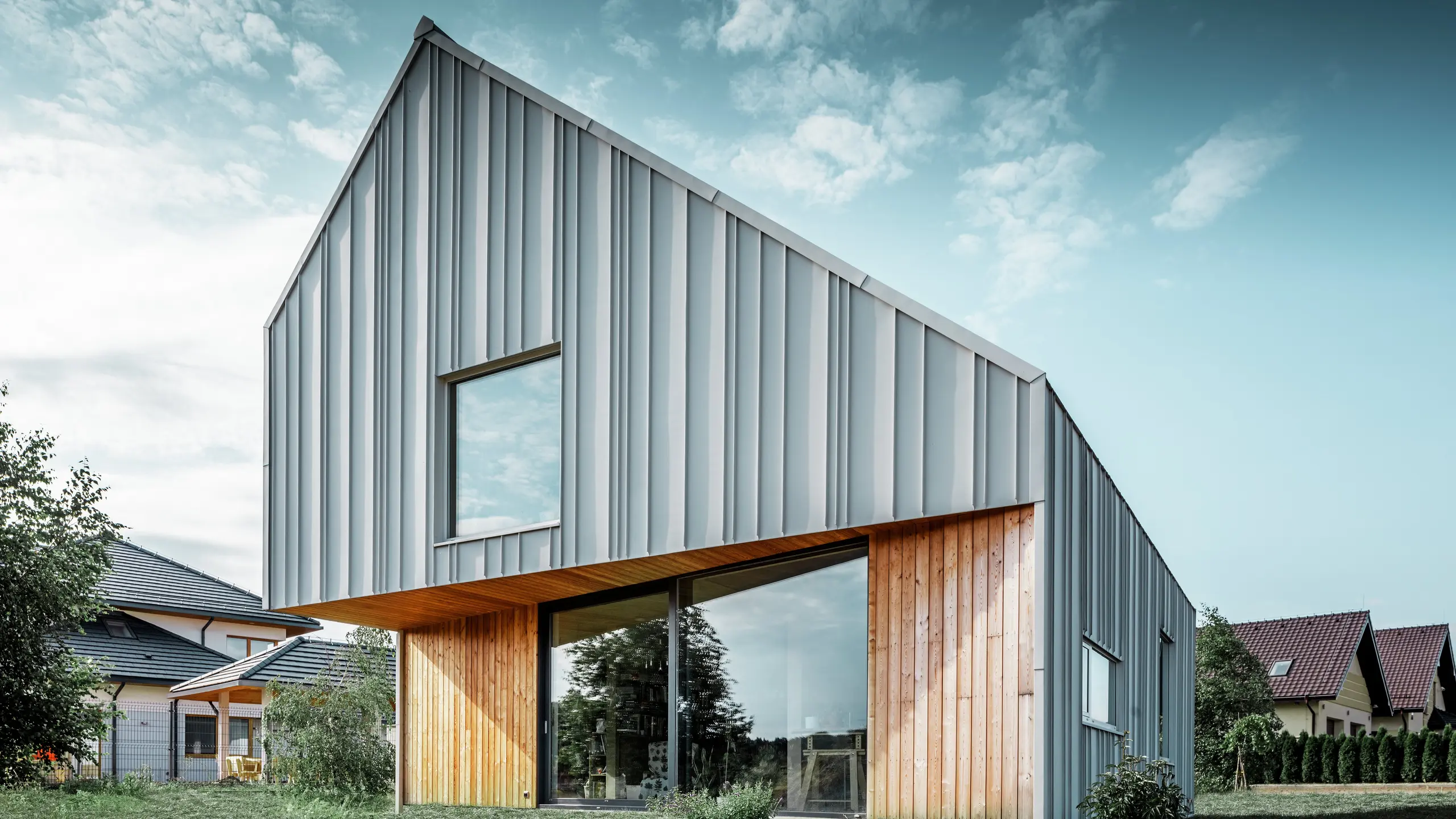 Modern vrijstaand huis met schuin dak zonder dakrand en aluminium gevel van PREFA in wit. Een houten gevel is gecombineerd met verticale houten panelen op de begane grond. 
