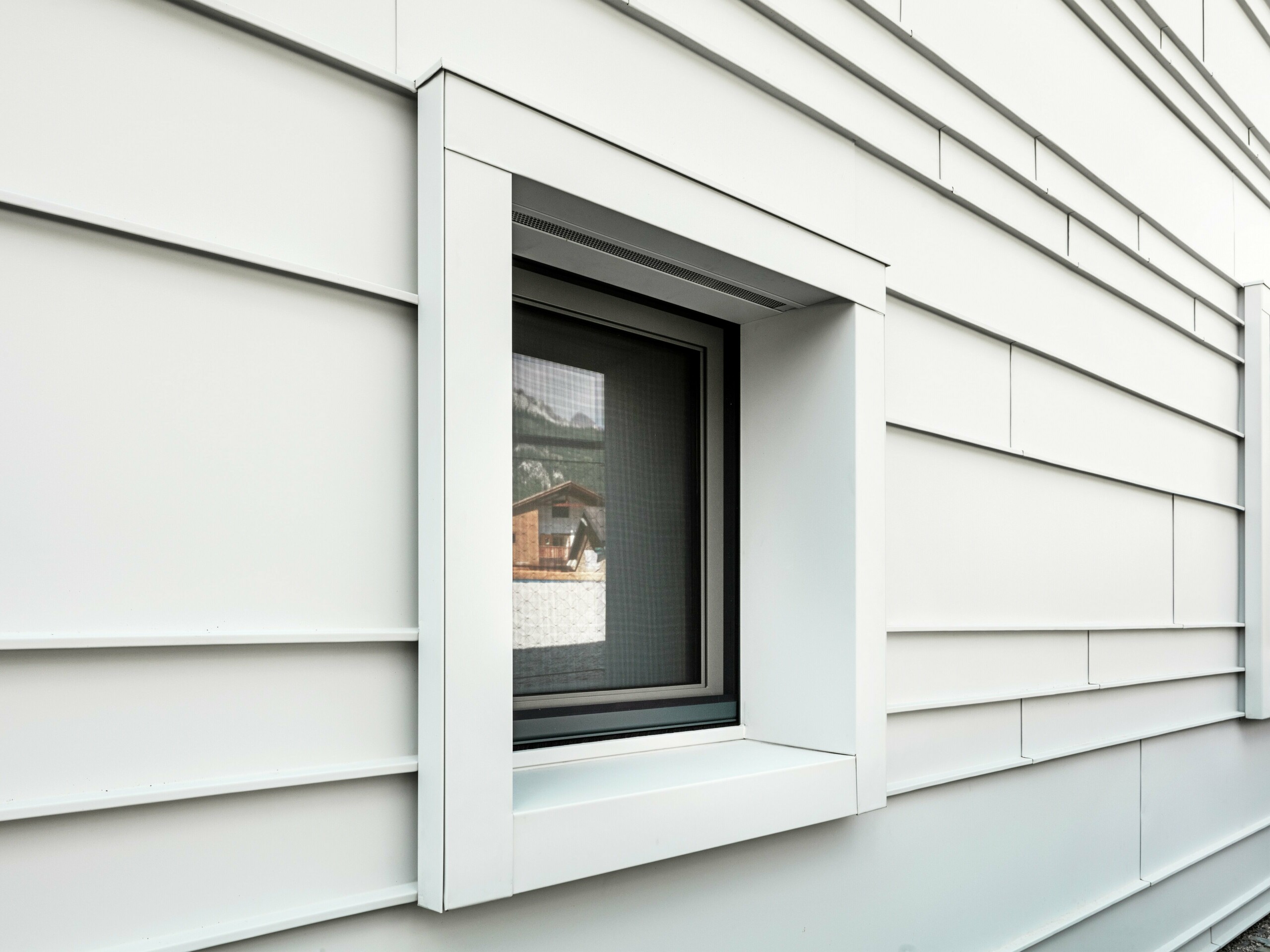 Détail d'une fenêtre caractéristique dans une façade ventilée en PREFALZ P.10 couleur blanc Prefa. Les lames d'aluminium posées horizontalement apportent structure, clarté et esthétique moderne. Les cadres de fenêtres très saillants de la caserne « Tempesti » commencent et se terminent toujours exactement au niveau d'une ligne de pli. Cela permet de mettre délibérément en valeur la structure de l'aluminium.