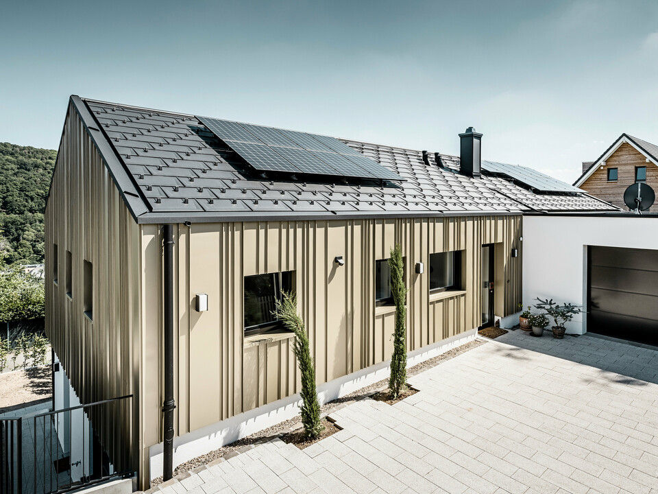 Ein Neubau in Bad Münstereifel wurde eingedeckt mit der PREFA Dachplatte R.16 in anthrazit. Auf dem Dach befindet sich eine Photovoltaik-Anlage. Die Winkelfalzfassade besteht aus Falzonal in lichtbronze.