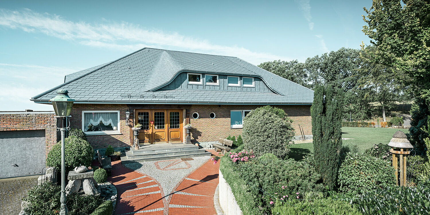 Eingangsbereich mit Vorgarten eines traditionellen Einfamilienhaus mit Dachgaube und PREFA Dachschindeln.