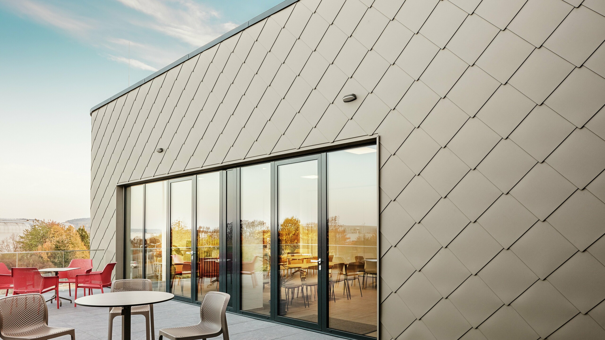 Die Fassade des neuen PREFA Standortes in Törökbálint besticht durch die eleganten PREFA Wandrauten 44 × 44 in P.10 Prefabronze. Die präzise verlegte Aluminiumfassade sorgt für ein modernes, dynamisches Erscheinungsbild und bietet gleichzeitig maximalen Schutz vor Witterungseinflüssen. Die großzügige Glasfront verbindet Innen- und Außenbereich und schafft auf der großzügigen Terrasse eine helle und einladende Atmosphäre.