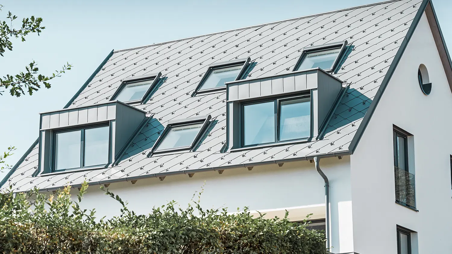 Dakrenovatie van een zadeldak met twee dakkapellen en vier dakramen, het dak is gedekt met de PREFA daklosange 44×44 in lichtgrijs. De goot is de PREFA hanggoot, eveneens in lichtgrijs. 