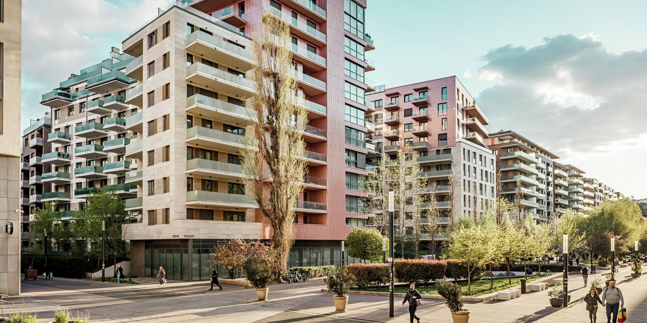 Une scène de rue le long de la promenade Corvin à Budapest, avec l'impressionnant complexe résidentiel Grand Corvin au premier plan. Les étages supérieurs sont revêtus de bardage PREFA, posé verticalement, dans une couleur saumon métallisée spéciale, apportant une touche de modernité à l'espace urbain. Ce revêtement en aluminium durable allie design, qualité et résistance aux intempéries dans l'un des plus grands projets de rénovation urbaine d'Europe centrale.