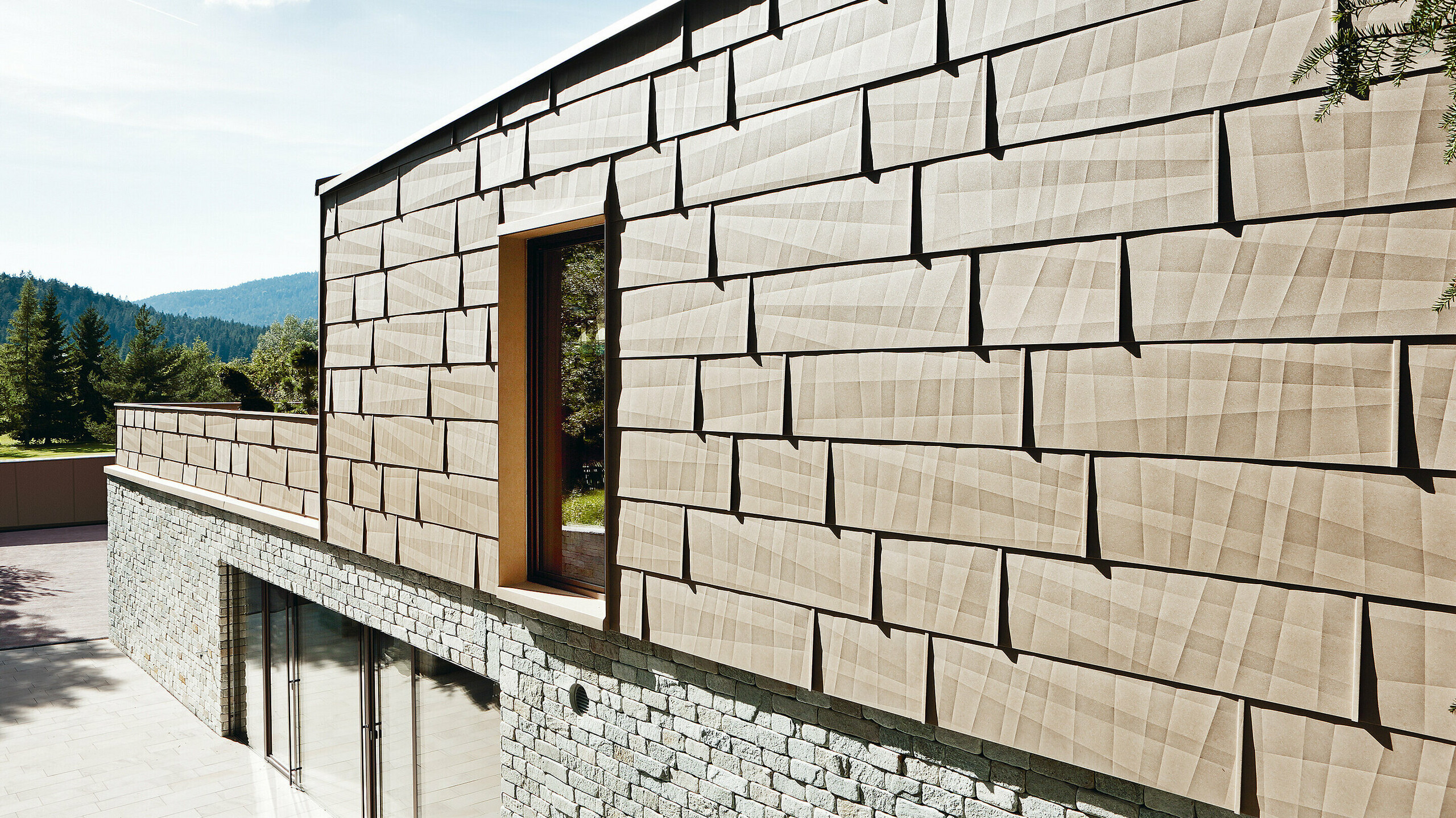 Façade combinant aluminium et pierre Sur cette façade extérieure, le panneau de façade FX.12 PREFA couleur P.10 brun sable est associé à une façade en pierre au rez-de-chaussée.