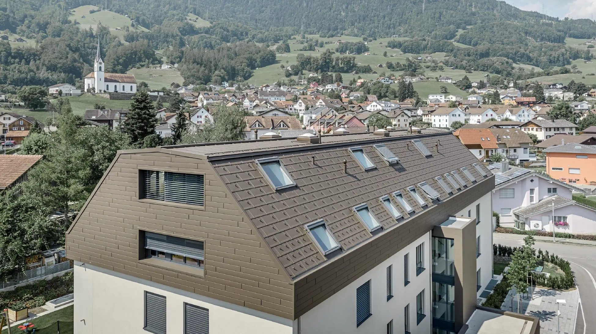 Les étages supérieurs de l’immeuble d’habitation ont été recouverts avec des Sidings et tuiles R.16 de PREFA couleur brun. De nombreuses fenêtres de toit sont visibles.