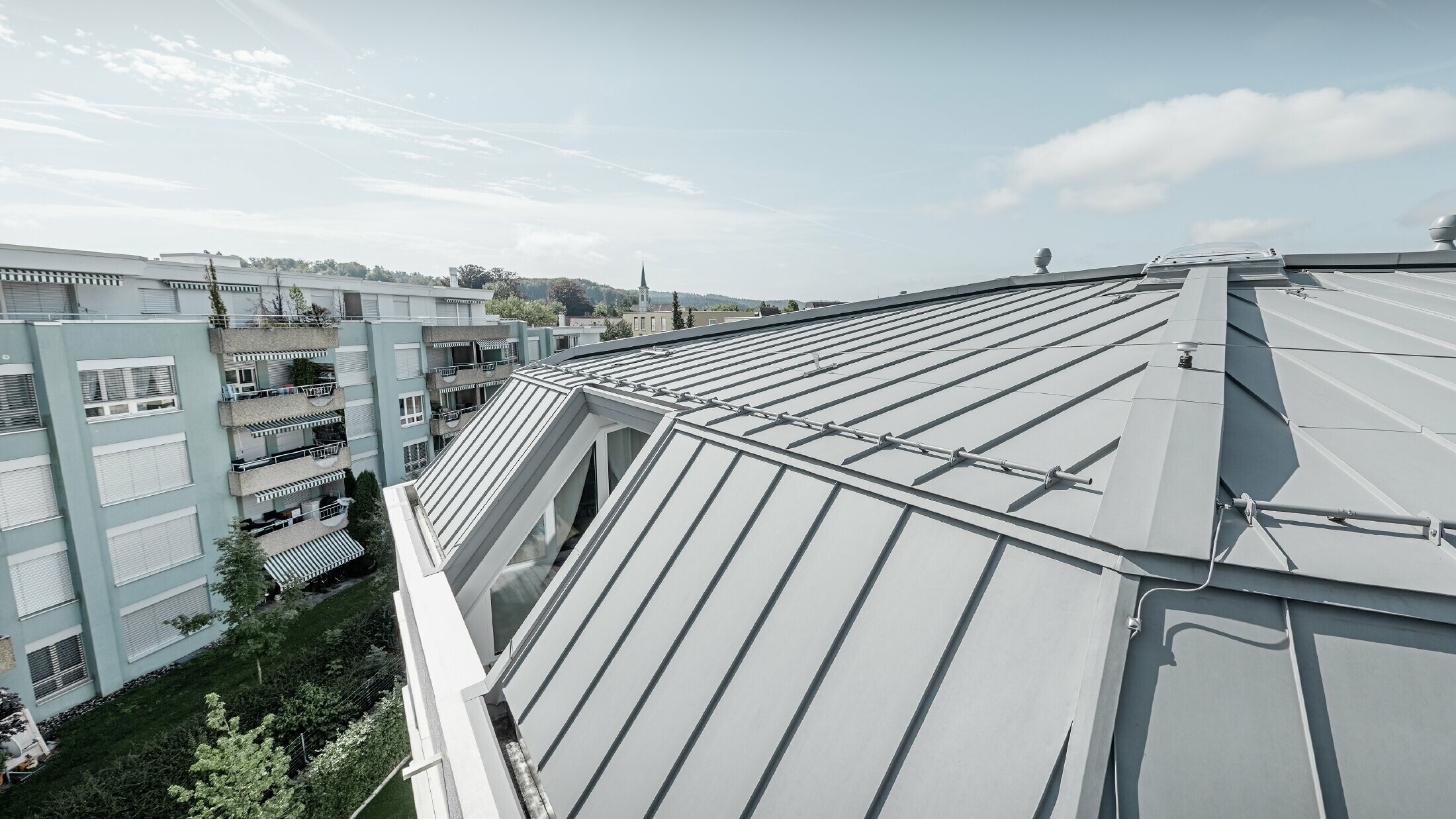 Detailbeeld van het dakvlak van een woongebouw; staand felsdak uitgevoerd in PREFA Prefalz in patinagrijs.