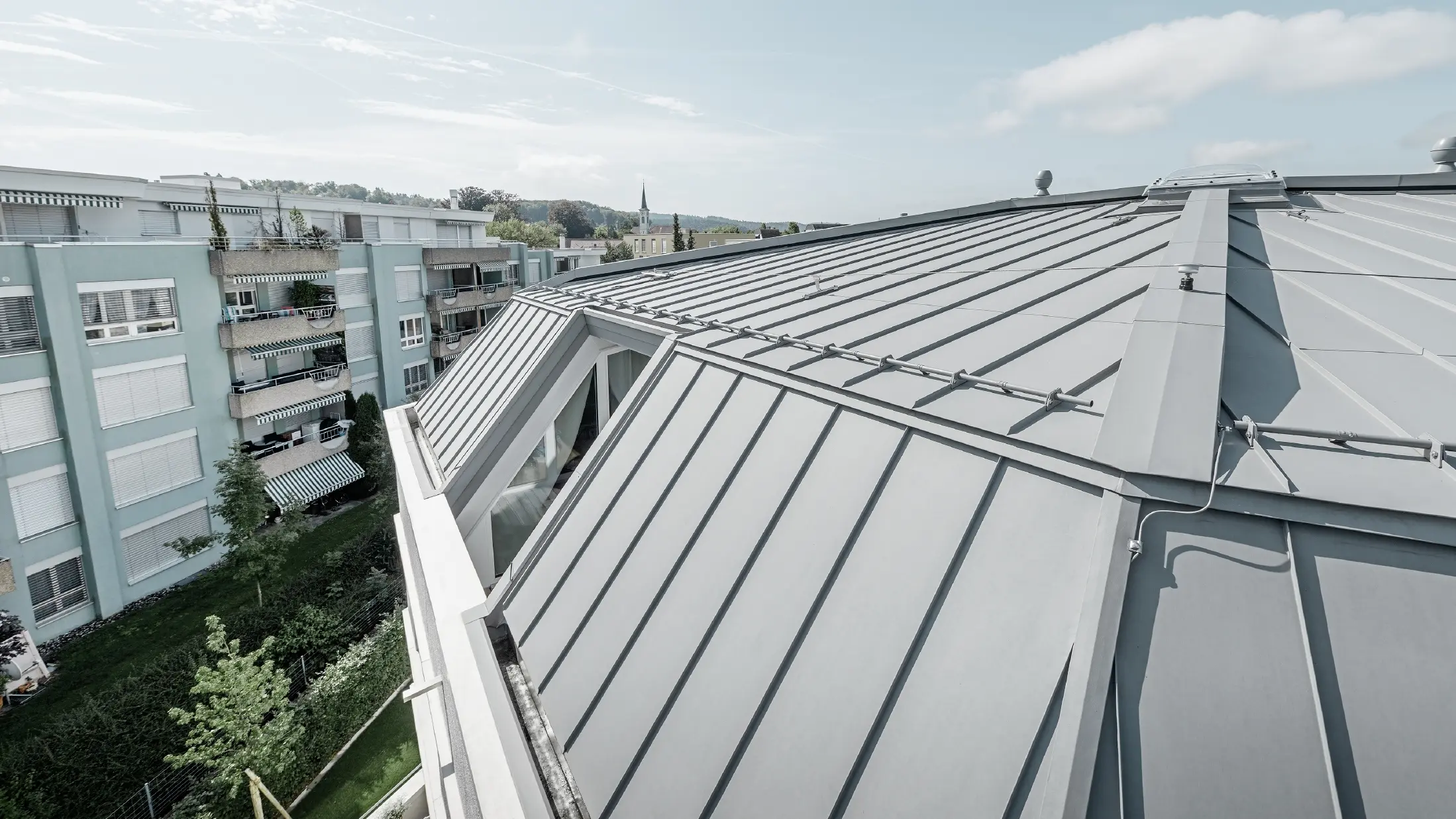 Detailbeeld van het dakvlak van een woongebouw; staand felsdak uitgevoerd in PREFA Prefalz in patinagrijs.