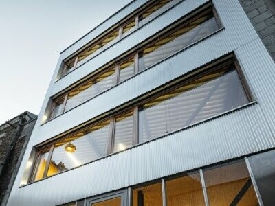 Vue du dessous des bureaux des architectes DLW, les reflets aluminium naturel des profils triangles scintillent dans la lumière du crépuscule.