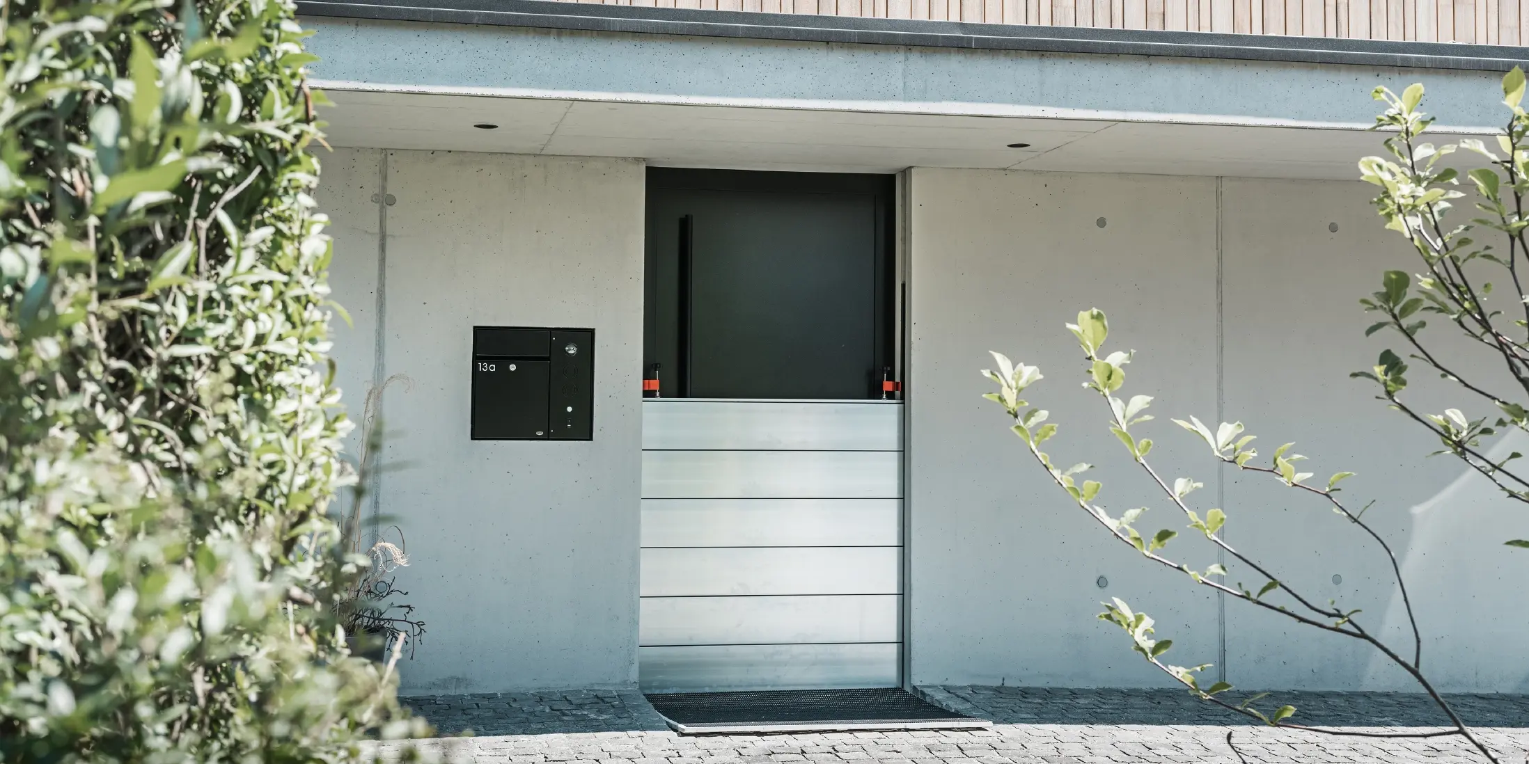 Vor der Eingangstür eines Einfamilienhauses mit Holzfassade wurde der PREFA Hochwasserschutz montiert. Die robusten Dammbalken aus Aluminium garantieren langfristige Sicherheit gegen Hochwasser und Schlamm.