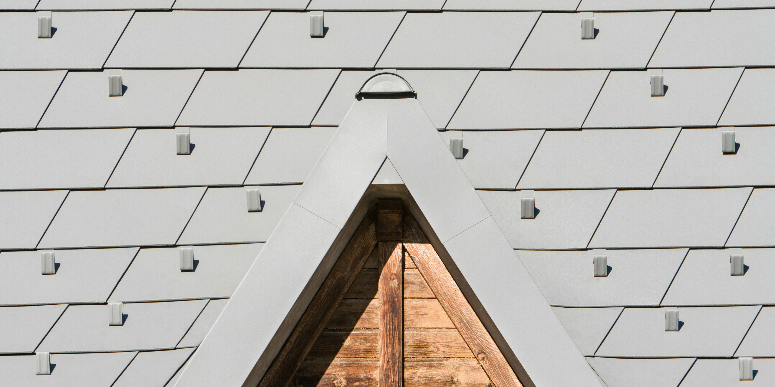 Vue détaillée des bardeaux de toiture PREFA en P.10 gris souris dans un projet de rénovation complexe à Barcelonnette, France.