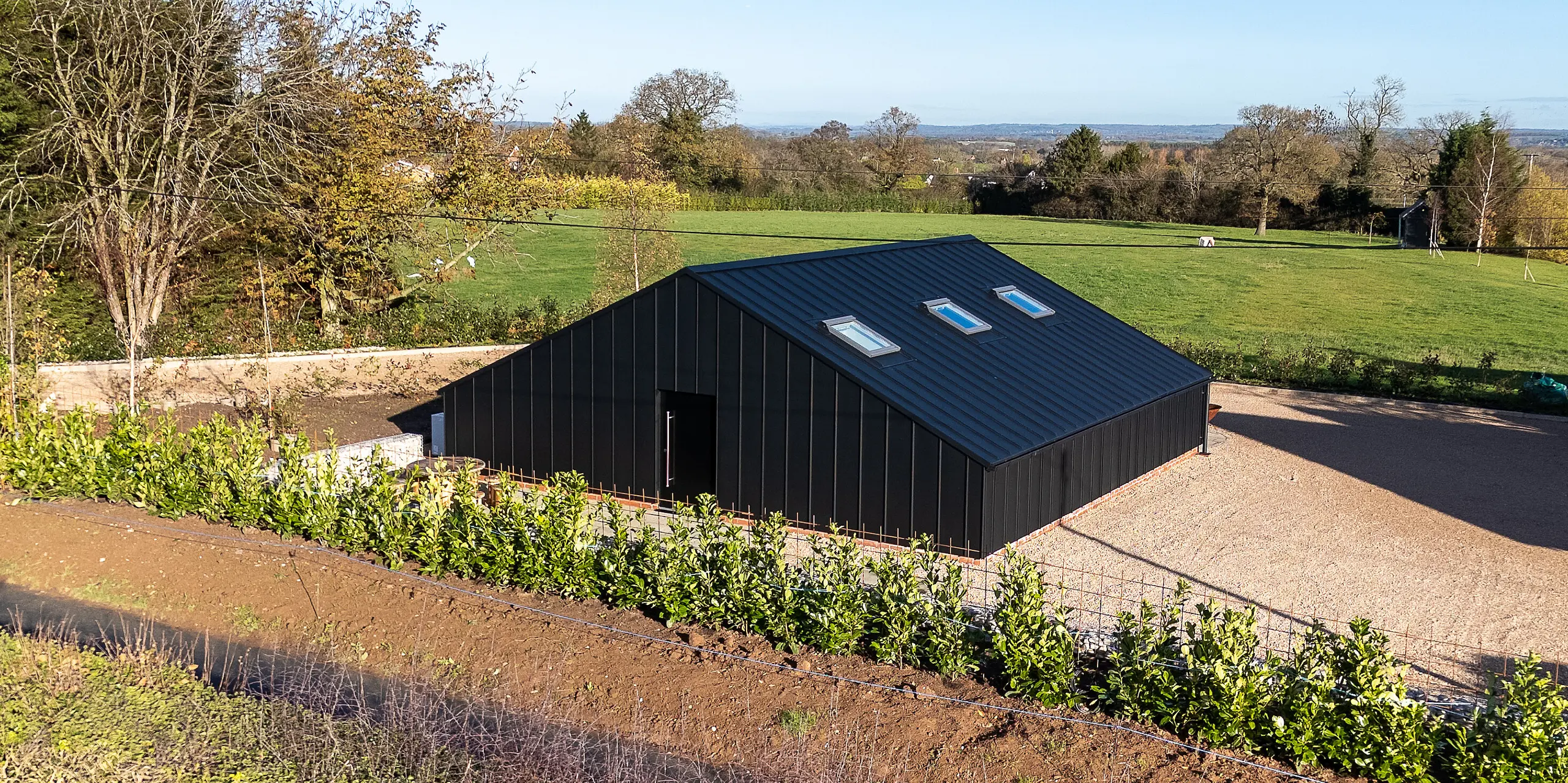 Vue arrière d'un bâtiment de loisirs moderne revêtu d'une façade en aluminium PREFA et d'une toiture PREFALZ P.10 Noir. La forme épurée et géométrique, ainsi que la surface homogène en aluminium, créent un contraste architectural avec le paysage environnant. Sa construction durable et résistante aux intempéries offre une protection maximale et une esthétique extérieure haut de gamme.