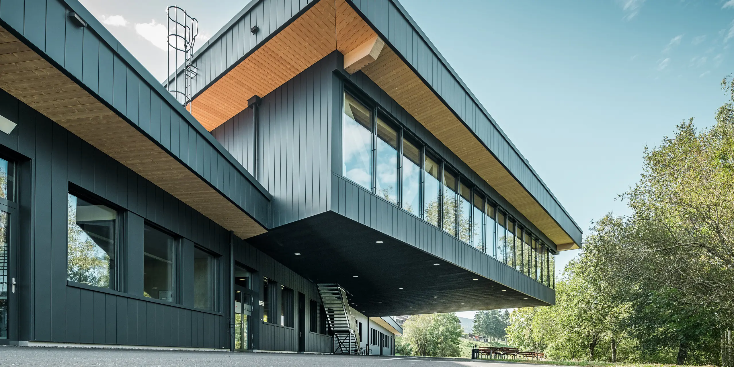 Modernes Firmengebäude von KIF Parechoc in Le Brassus mit eindrucksvoll auskragendem Obergeschoss und vertikal verlegten PREFA Sidings in P.10 Anthrazit. Die markante Aluminiumfassade bildet gemeinsam mit den großflächigen Verglasungen und warmen Holzuntersichten einen spannenden Kontrast. PREFA Sidings überzeugen durch Langlebigkeit, Korrosionsbeständigkeit und ihre besonders wartungsarme Oberfläche.