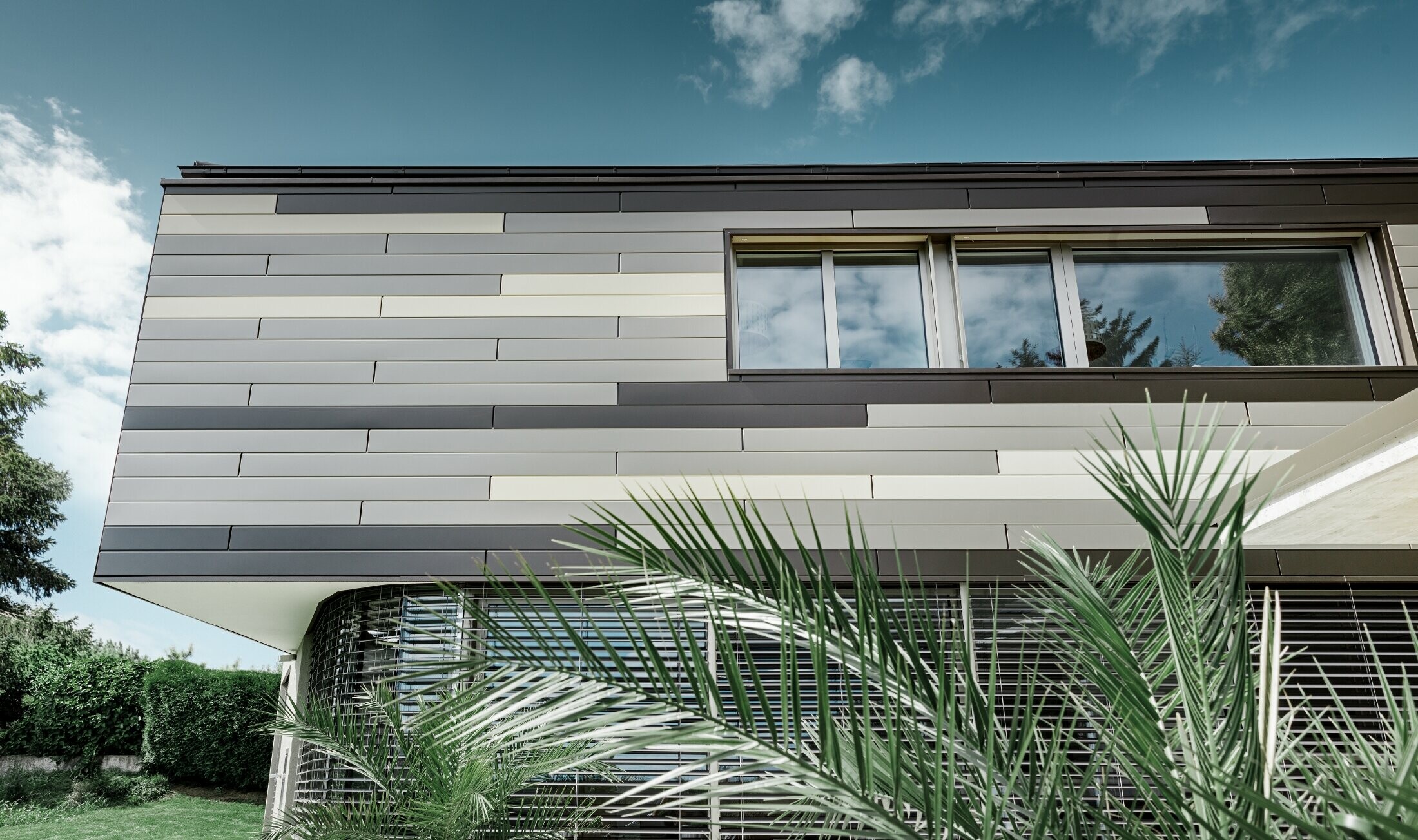 Modernes Einfamilienhaus mit Flachdach und überdachter Terrasse mit einer individuell gestalteten Aluminiumfassade aus Sidings in braun, bronze und elfenbein von PREFA