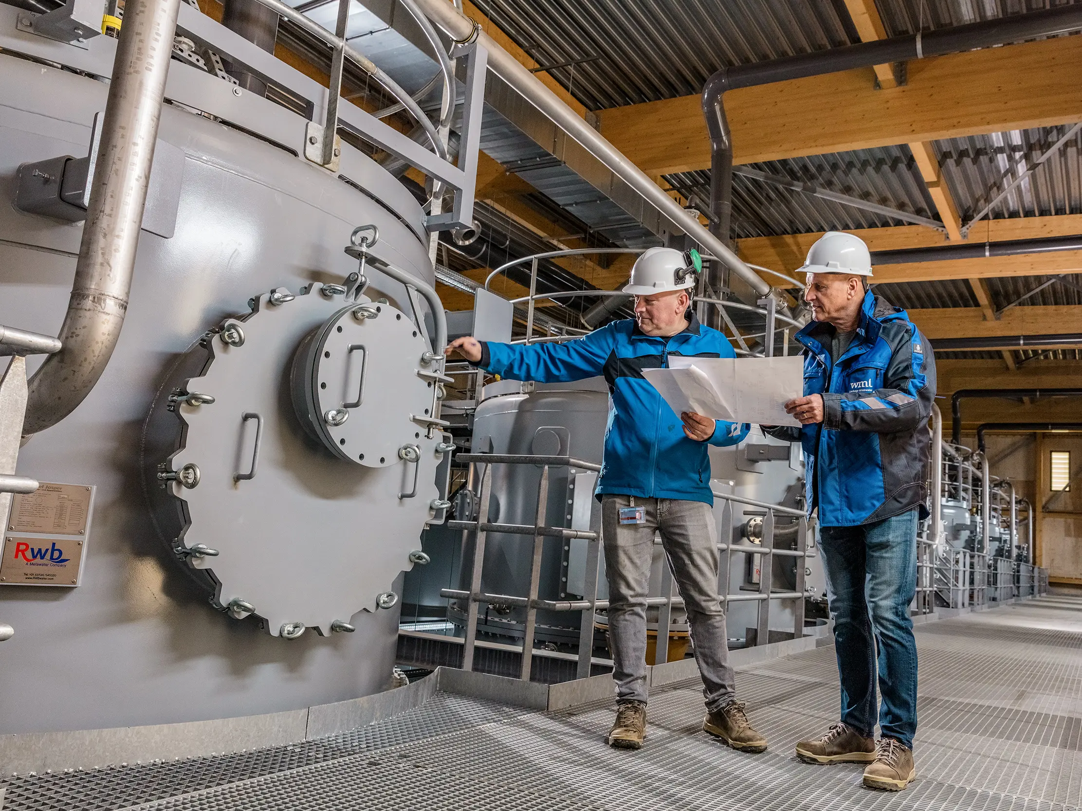 Dans la station de pompage d'eau potable ultramoderne de WML à Lottum, deux spécialistes œuvrent au milieu de systèmes de filtration à grande échelle, de canalisations et d'installations de précision, sous une remarquable structure en bois. L'accent est mis sur la robustesse des réservoirs cylindriques et la clarté industrielle de l'espace. L'architecture performante se distingue par ses façades extérieures en aluminium PREFA, durables et élégantes, qui impressionnent par leur légèreté, leur grande résistance aux intempéries et leur recyclabilité. L'alliance de la haute technologie, du bois et de matériaux innovants fait de ce bâtiment une infrastructure avant-gardiste et remarquable.