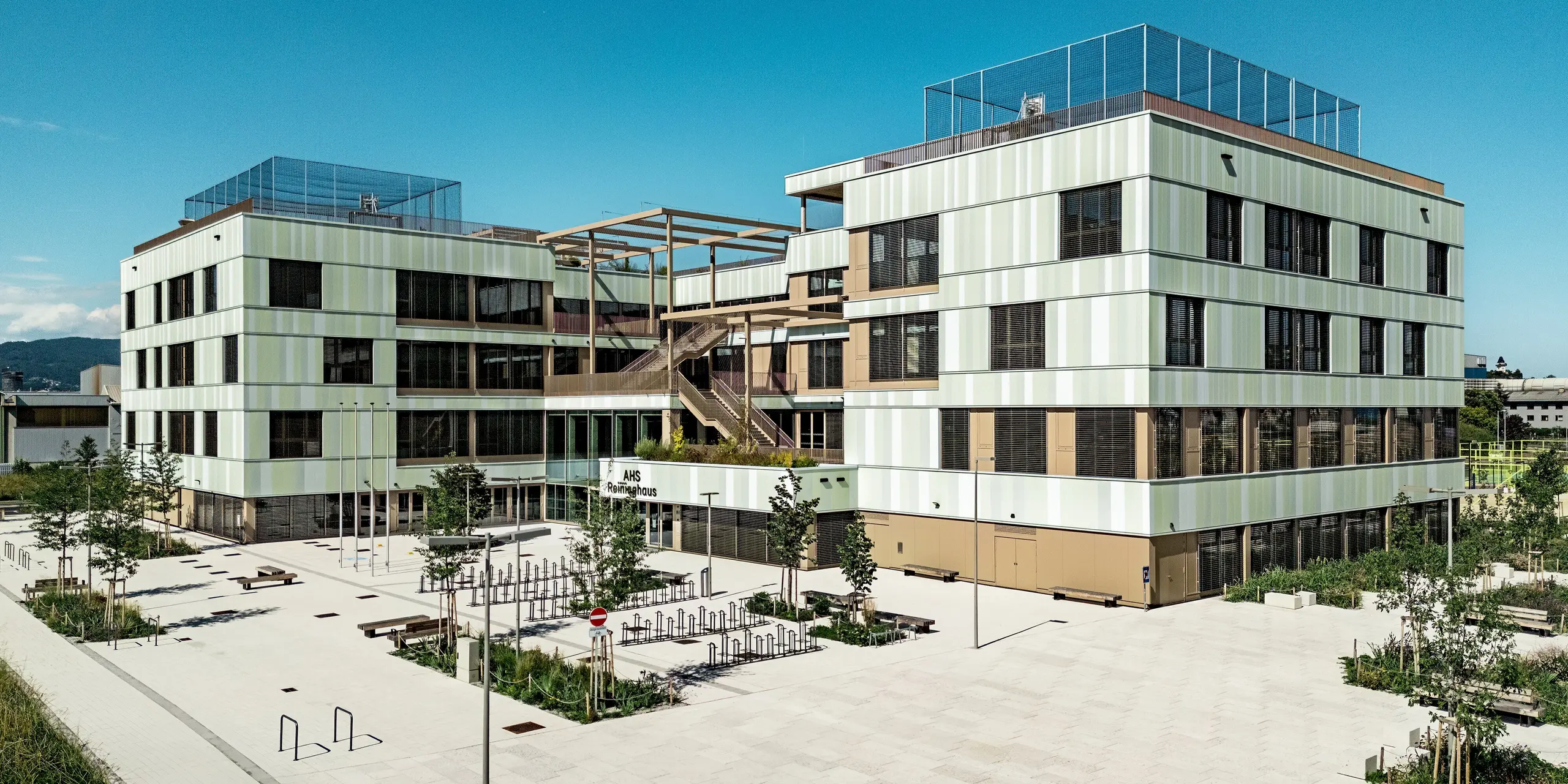 Die AHS Reininghaus in Graz begeistert mit ihrer modernen Architektur, die durch die PREFA Sidings in Sonderfarben hervorgehoben wird. Die Fassadenverkleidung aus Aluminium in sanften Grün- und Weißtönen sorgt für ein frisches, elegantes Erscheinungsbild. Besonders auffällig ist die gelungene Kombination aus der strukturierten Fassade und den Fensterläden, die das Gebäude sowohl optisch aufwerten als auch für Privatsphäre und Sonnenschutz sorgen. Diese Kombination aus ästhetischem Design und langlebiger Materialqualität garantiert eine funktionale, pflegeleichte und energieeffiziente Lösung, die im städtischen Umfeld von Graz herausragt.