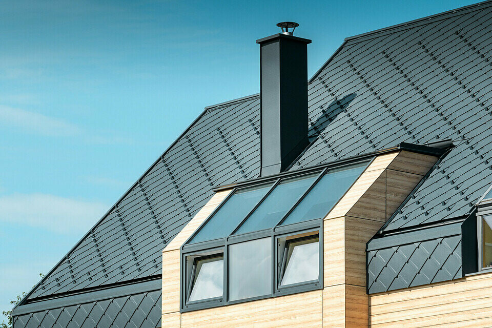 Maison individuelle au toit à deux versants sans saillie de toit — Façade à l’aspect du bois et toiture en aluminium PREFA de couleur anthracite