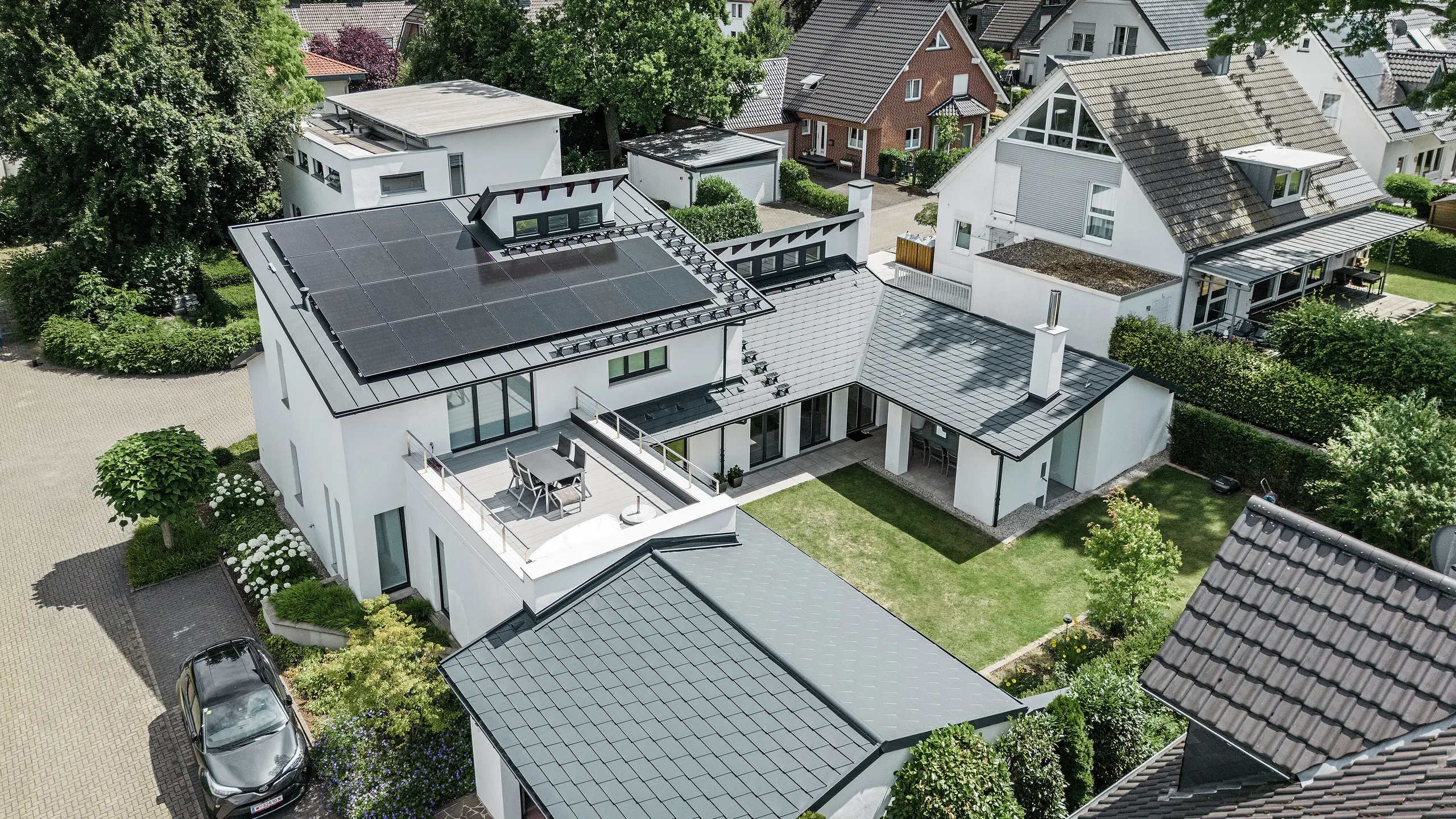 Uitzicht in vogelvlucht op het markante daklandschap van een eengezinswoning in Dortmund met PREFA dakshingles DS.19 en PREFALZ in P.10 antraciet en een grootschalige PV-installatie