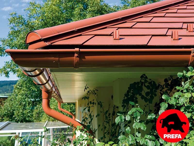 Maison individuelle avec toit à croupes et lucarne recouverte avec le bardeau PREFA en aluminium imitation tuile, rouge tuile