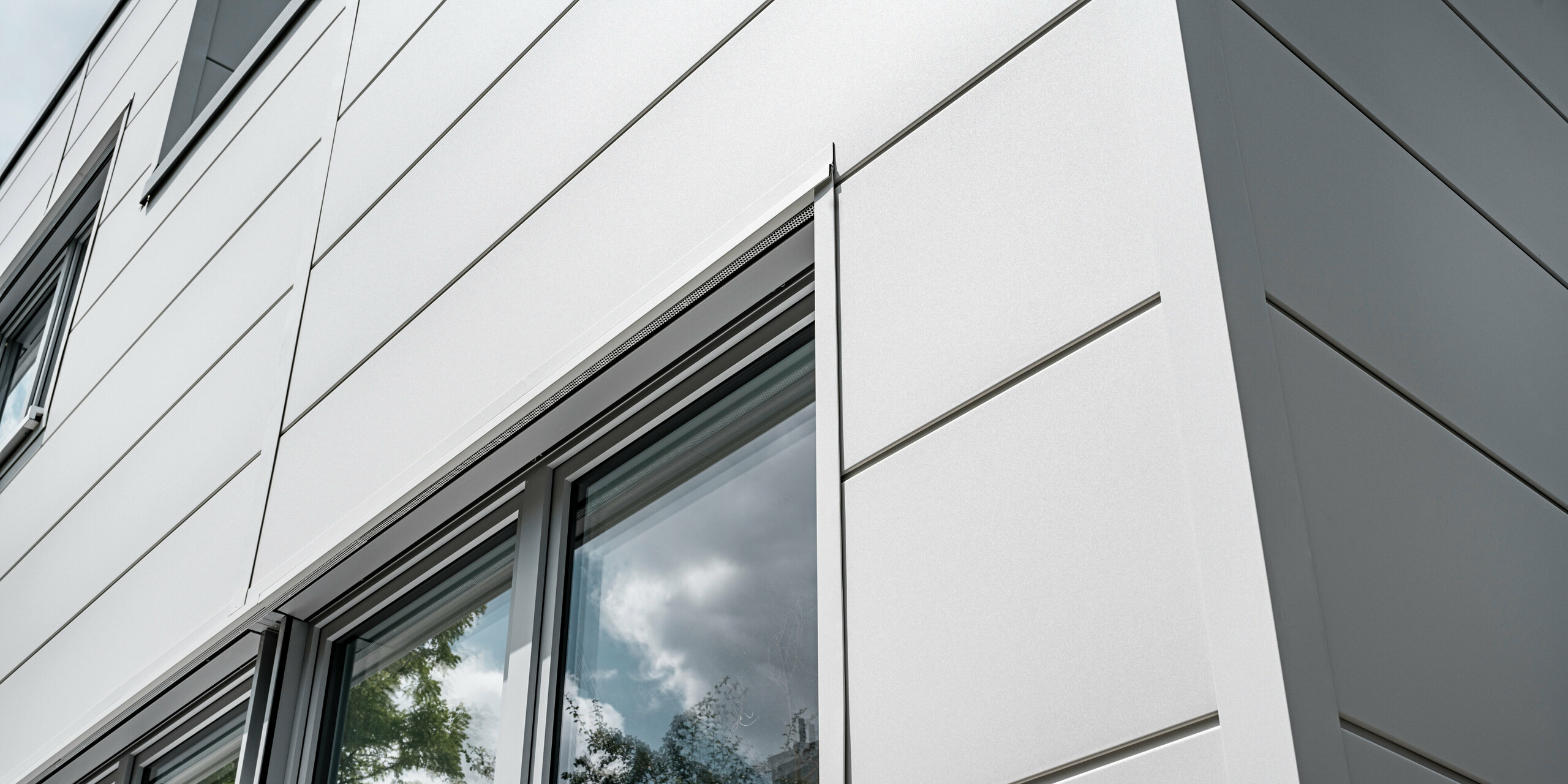 Des Sidings PREFA grand format entourent un bâtiment d'entreprise à Oberschleißheim (Allemagne). Les éléments de façade extra-larges en aluminium ont été choisis dans la couleur blanc Prefa.