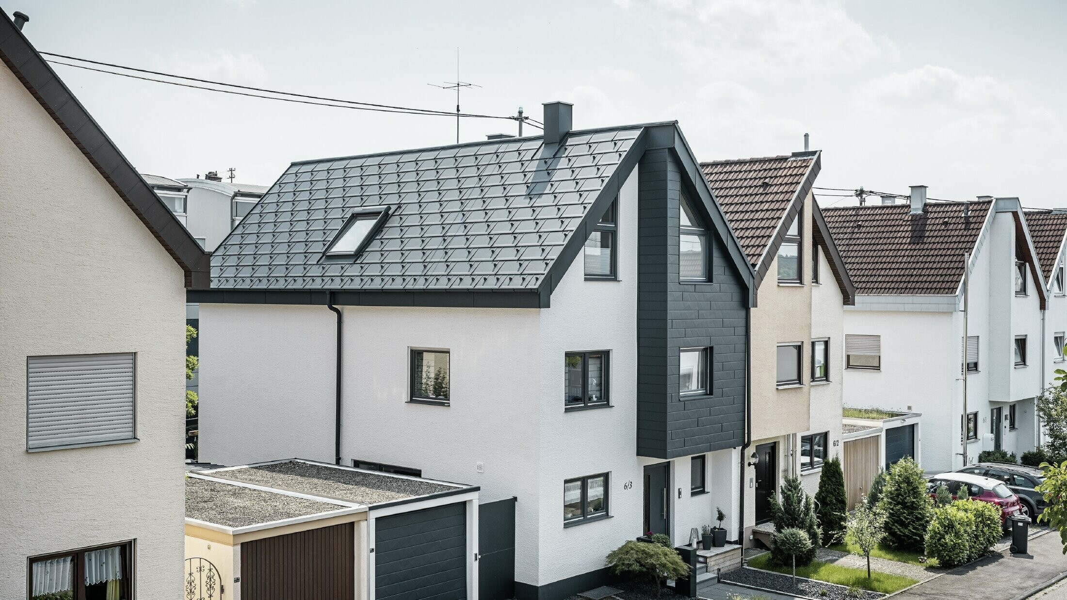 La moitié d'une maison jumelée a déjà été rénovée, avec une façade fraîchement crépie de blanc, combinée à une façade avec Siding.X PREFA en anthracite. Le toit est recouvert du R.16 PREFA. L'écoulement des eaux de pluie se fait par la gouttière carrée et le tuyau de descente PREFA.