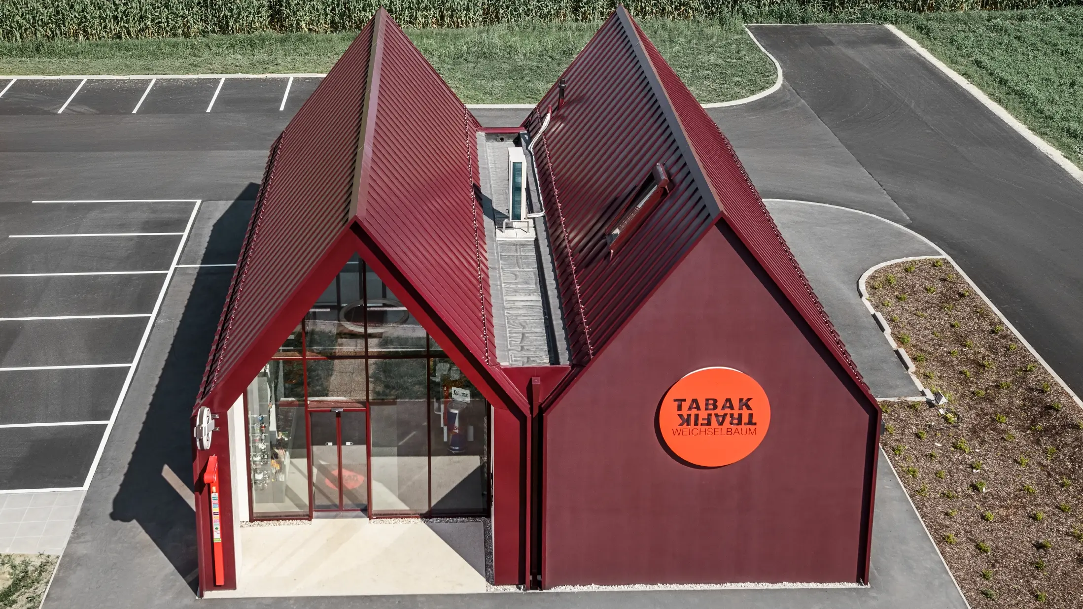 Bureau de tabac moderne au toit à deux versants sans saillie de façade — Enveloppe en aluminium PREFA à joints debout et joints angulaires rouge-noir (couleur spéciale)