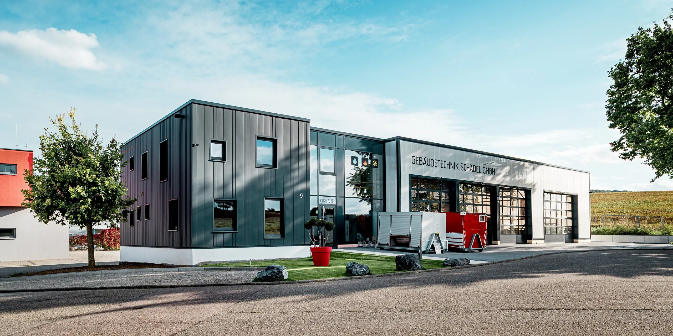 Vue d'ensemble, l'architecture du bâtiment de Schädel GmbH, entreprise spécialisée dans les technologies du bâtiment, se distingue par son aspect particulièrement imposant. Le Siding PREFA anthracite confère à la façade une allure épurée et structurée, en parfaite harmonie avec l'architecture industrielle moderne. L'association avec le soubassement clair et la large façade vitrée crée un contraste saisissant. Les profilés en aluminium résistant aux intempéries garantissent une esthétique durable et une protection optimale.